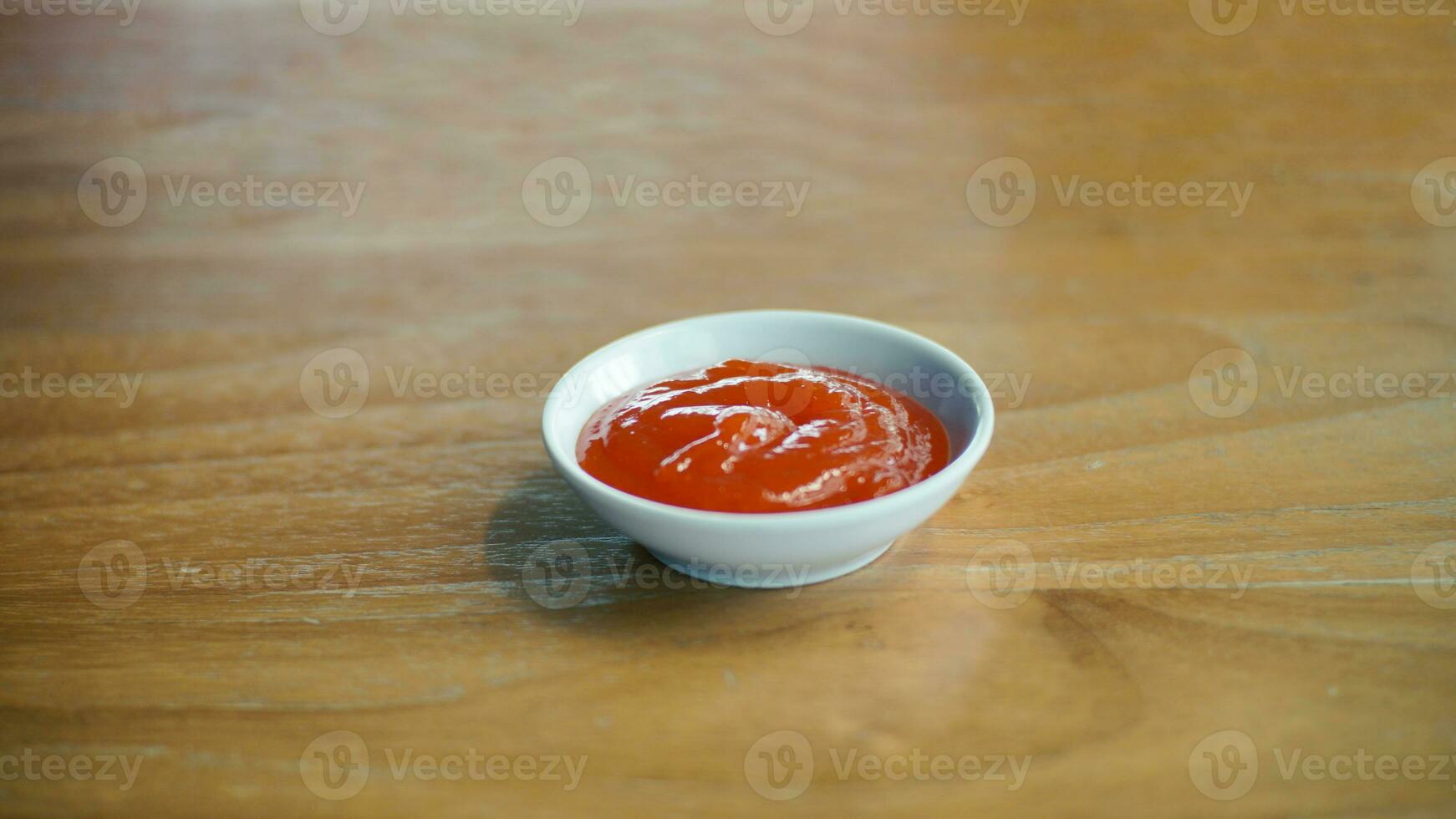 picante rojo salsa en un pequeño blanco cuenco en un de madera mesa en un restaurante. foto