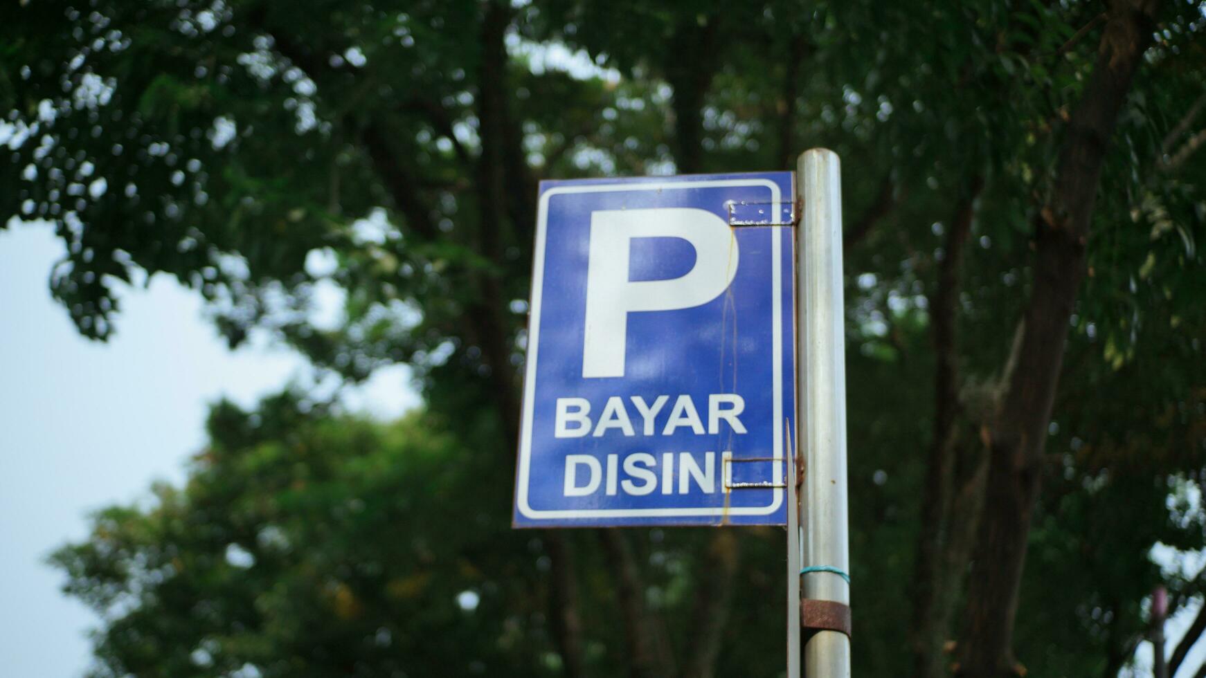 The vehicle parking sign says ''bayar disini'' which means ''pay here'' to pay for parking on the side of the road in Bandung. photo