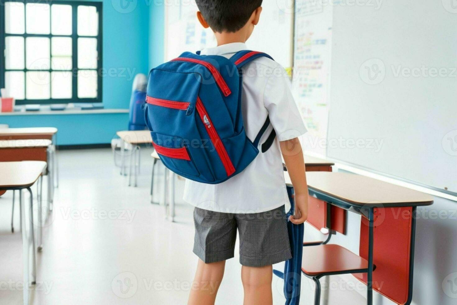 Back view of a schoolboy with a backpack standing in the classroom. Pro Photo