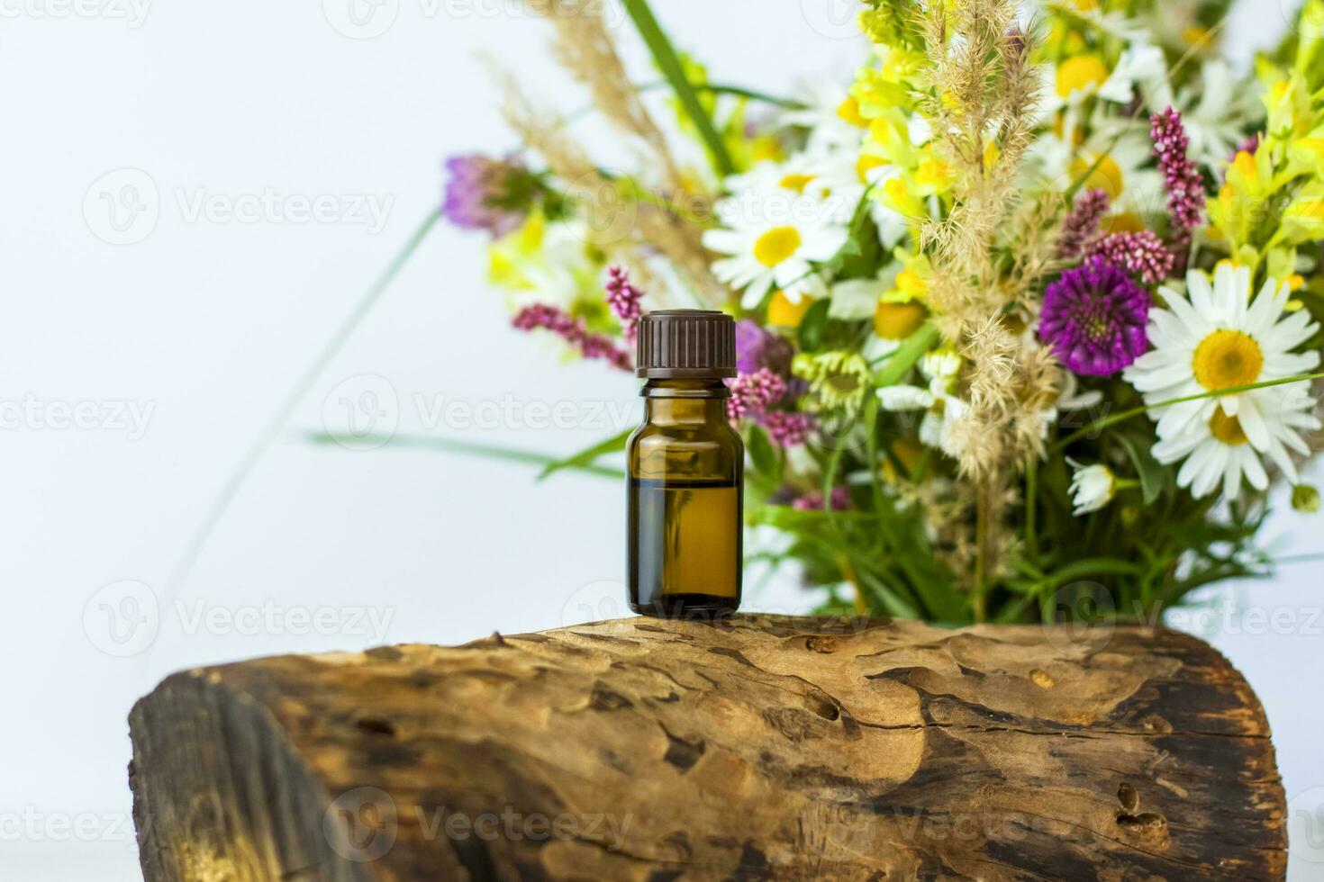 a bottle of cosmetic oil on the background of a dry stump, tree bark and a bouquet of wild flowers. Stylish appearance, layout, personality. Banner, a place for the text photo