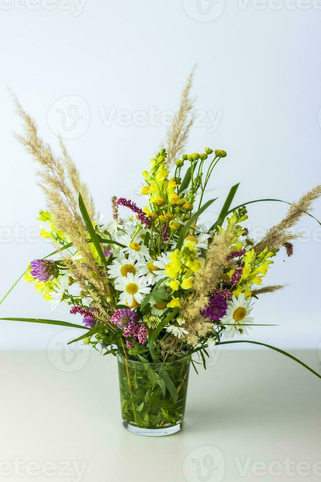 A bouquet of wild flowers in a small glass vase on a white background. Stylish appearance, layout, personality. Banner, a place for the text photo