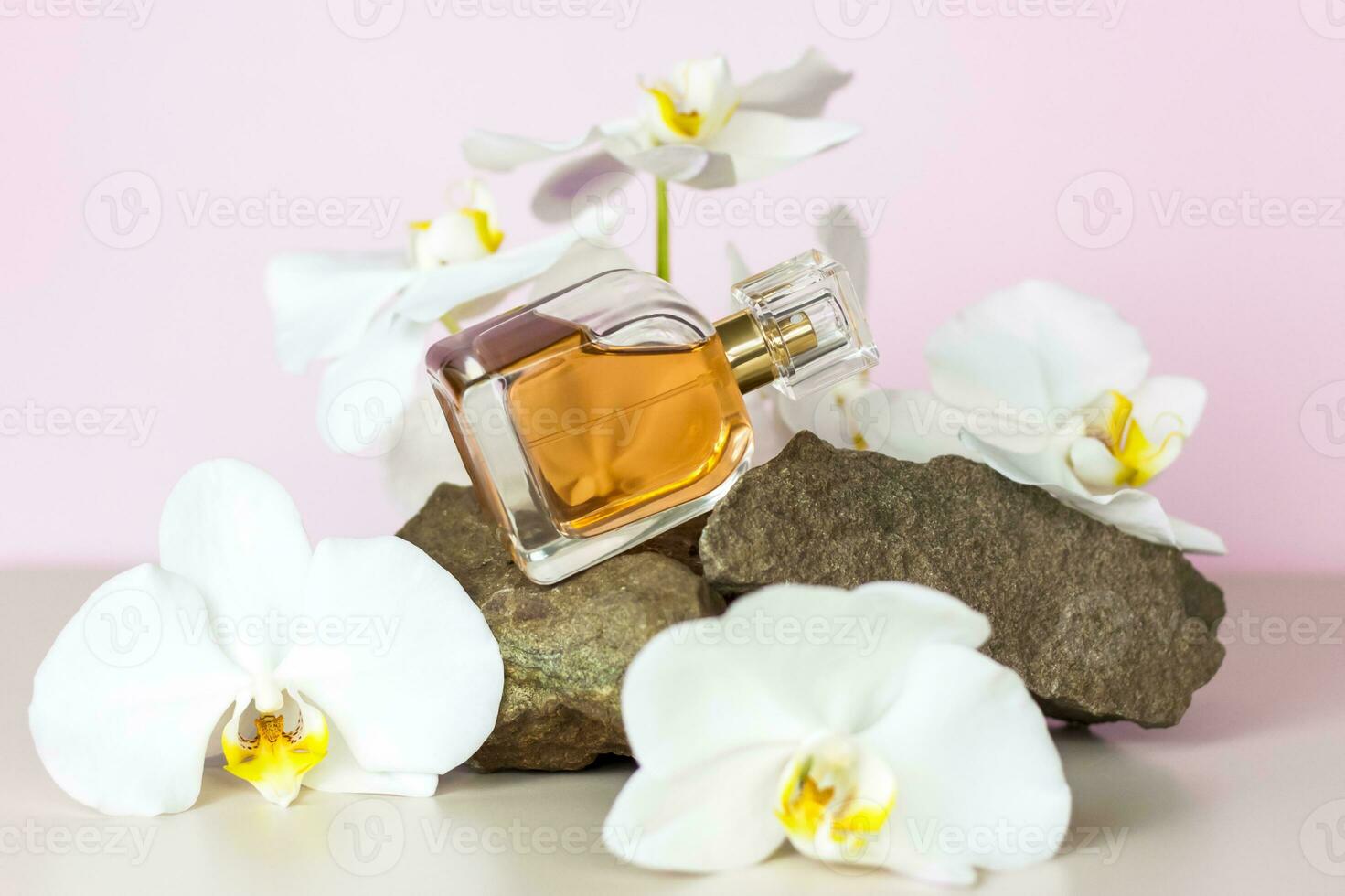 A perfume bottle stands on a stone against a background of beautiful orchids. Stylish appearance, layout, personality. Banner, a place for the text. photo