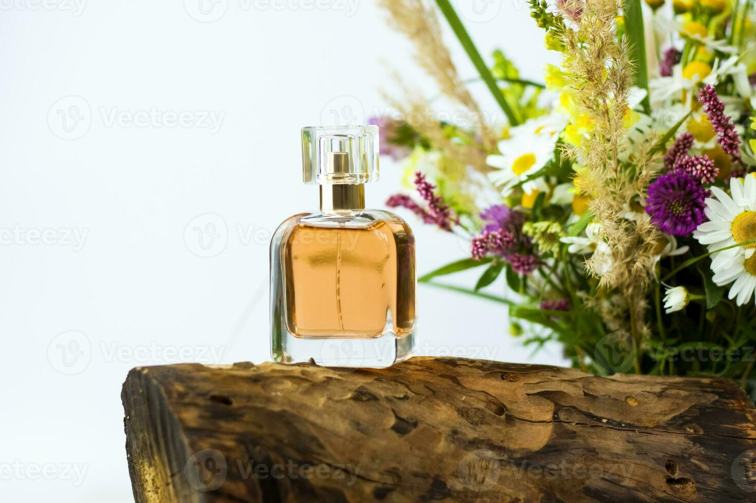 a perfume bottle on the background of a dry stump, tree bark and a bouquet of wild flowers. Stylish appearance, layout, personality. Banner, a place for the text. photo