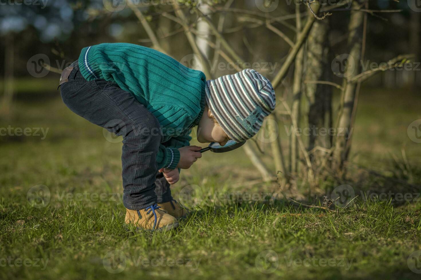 A funny boy walks through the spring park, examines the leaves with a large magnifying glass, looks for bugs and enjoys. photo