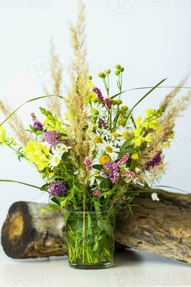 a dry stump, tree bark and a bouquet of wild flowers in a small glass vase. Stylish appearance, layout, personality. photo