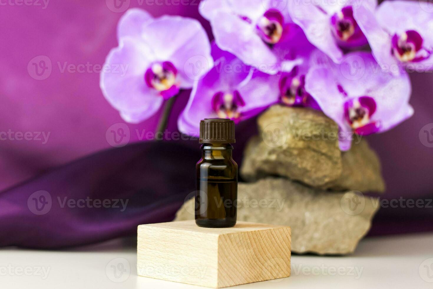 A bottle of cosmetic oil stands on a wooden pedestal against a background of stone and beautiful orchids. Stylish appearance of the product, layout, personality. Banner, a place for the text. photo