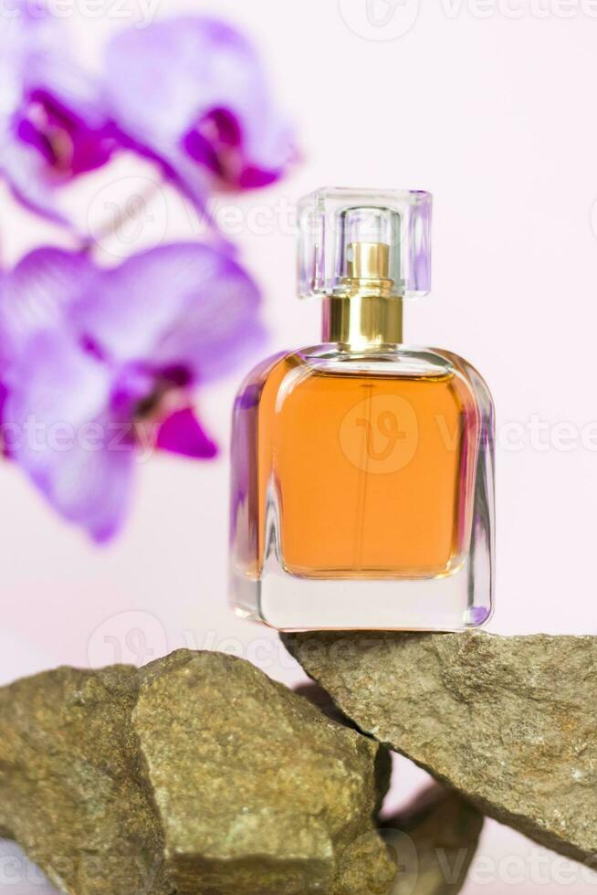 A perfume bottle stands on a stone against a background of beautiful orchids. Stylish appearance, layout, personality. Banner, a place for the text. photo