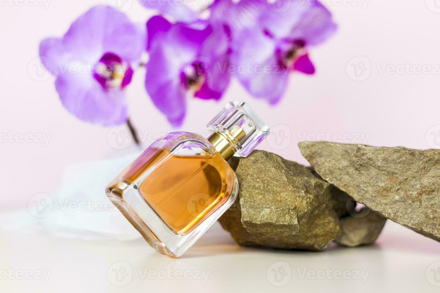 A perfume bottle stands on a stone against a background of beautiful orchids. Stylish appearance, layout, personality. Banner, a place for the text. photo