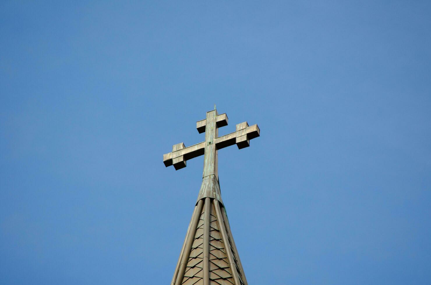 cruzar en pie en un Iglesia techo ,geométrico figura consistente de dos intersectando líneas o barras en contra el azul cielo. foto