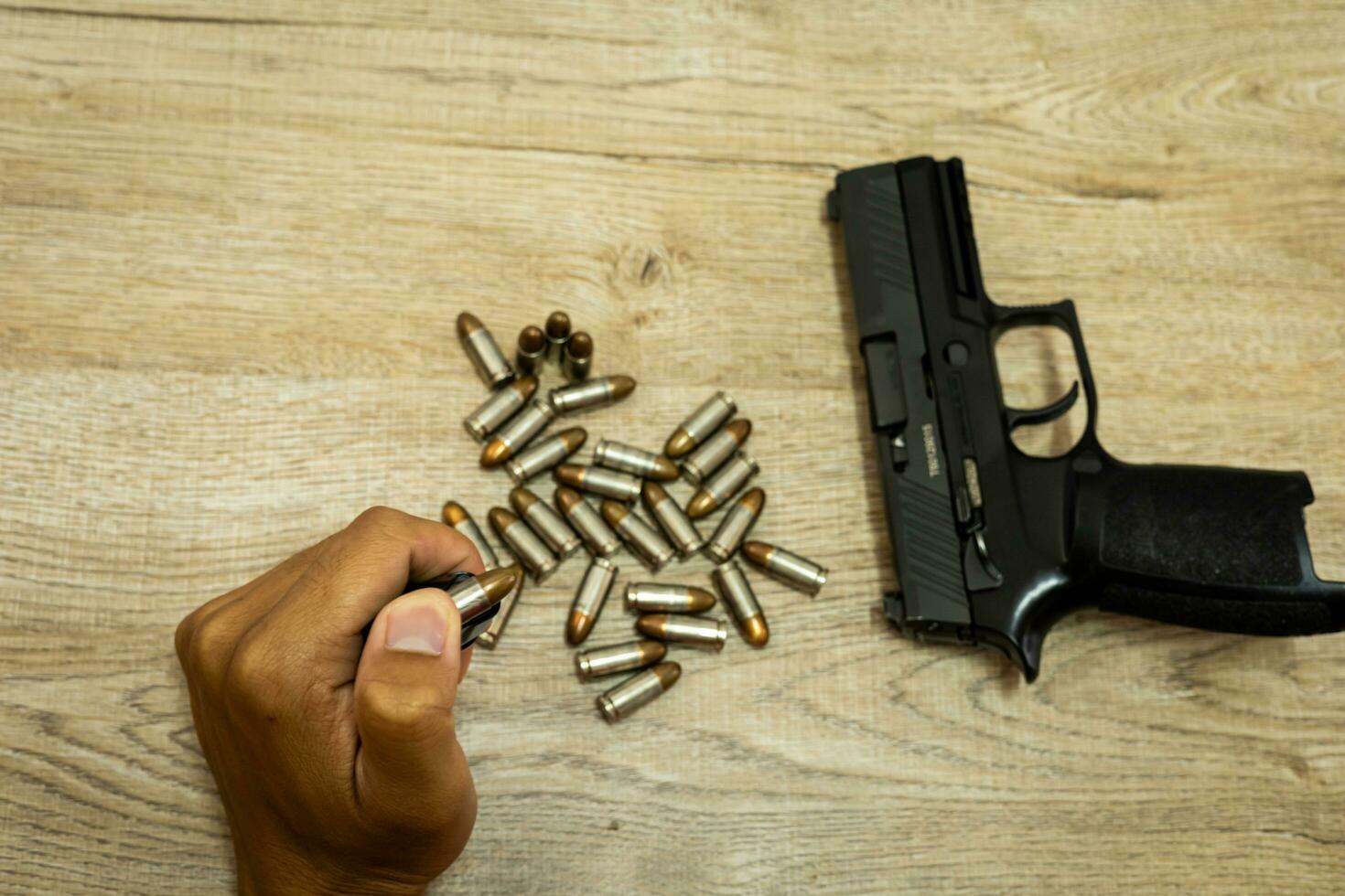 Male hand holding a bullet There's a pistol behind it, on a wooden table. photo