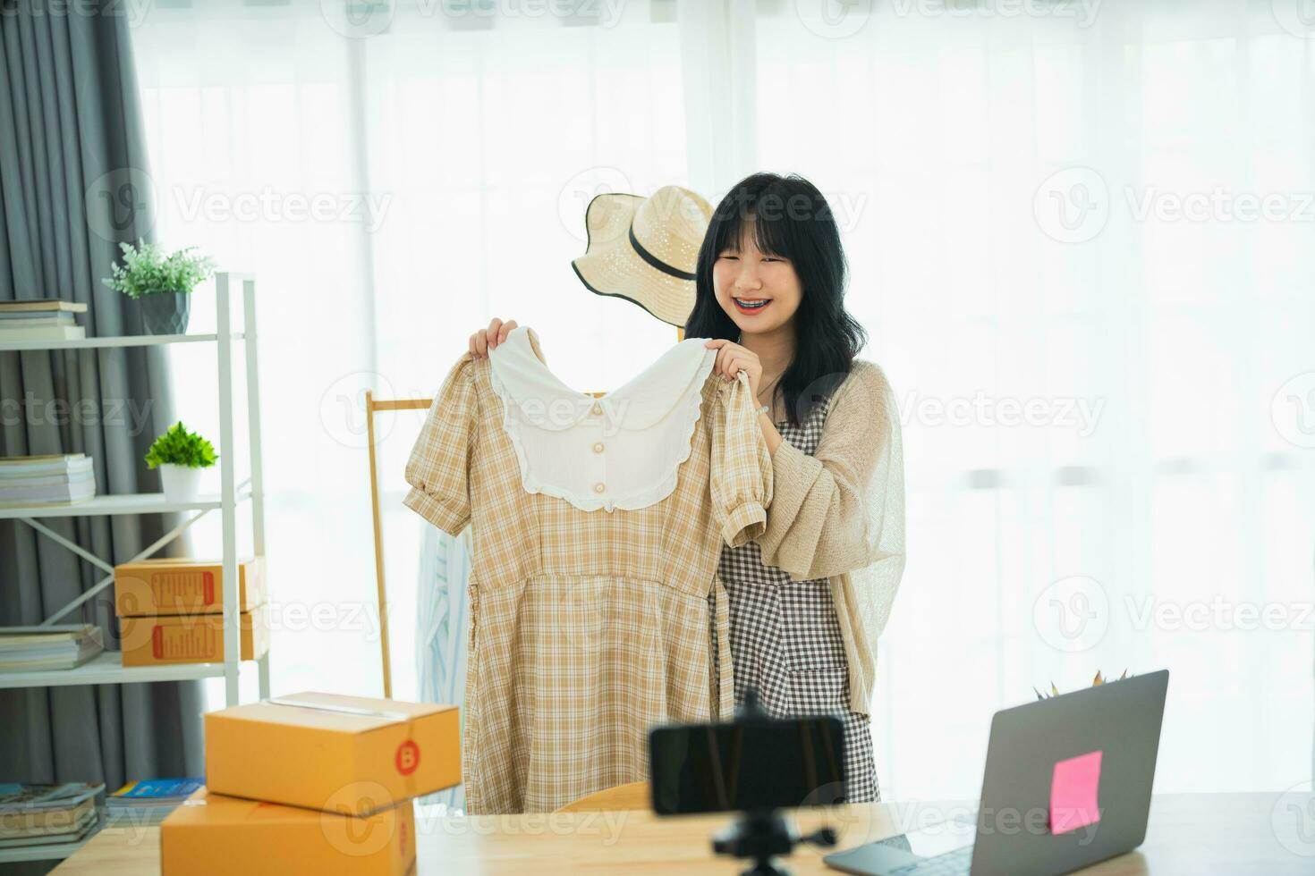 Asian woman steamming sell cloth shirt product online live at home. Young woman using mobile phone video call shows goods to customer and detail. Shopping online e-commerce buying and selling concept. photo