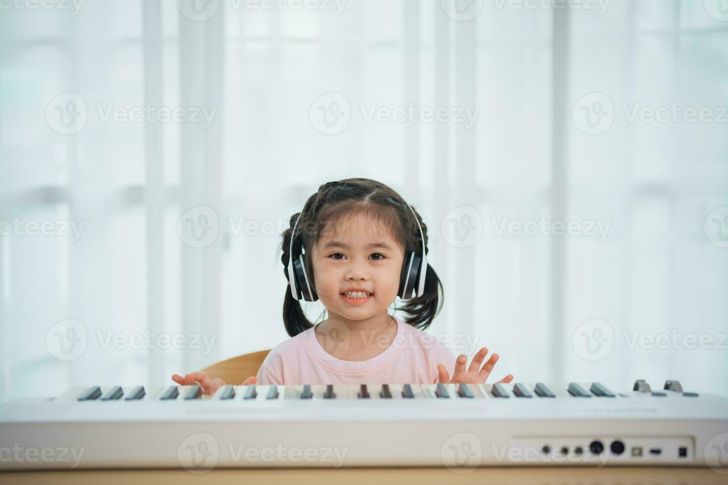 Asian cute girl smile and wearing white headphone playing learning online piano music in the living room at home. The idea of activities for the child at home during quarantine. Music learning study. photo