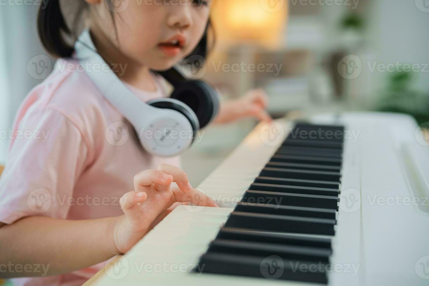 Close up. Asian cute girl smile wearing white headphone playing learning online piano music in living room at home. The idea of activities for child at home during quarantine. Music learning study. photo