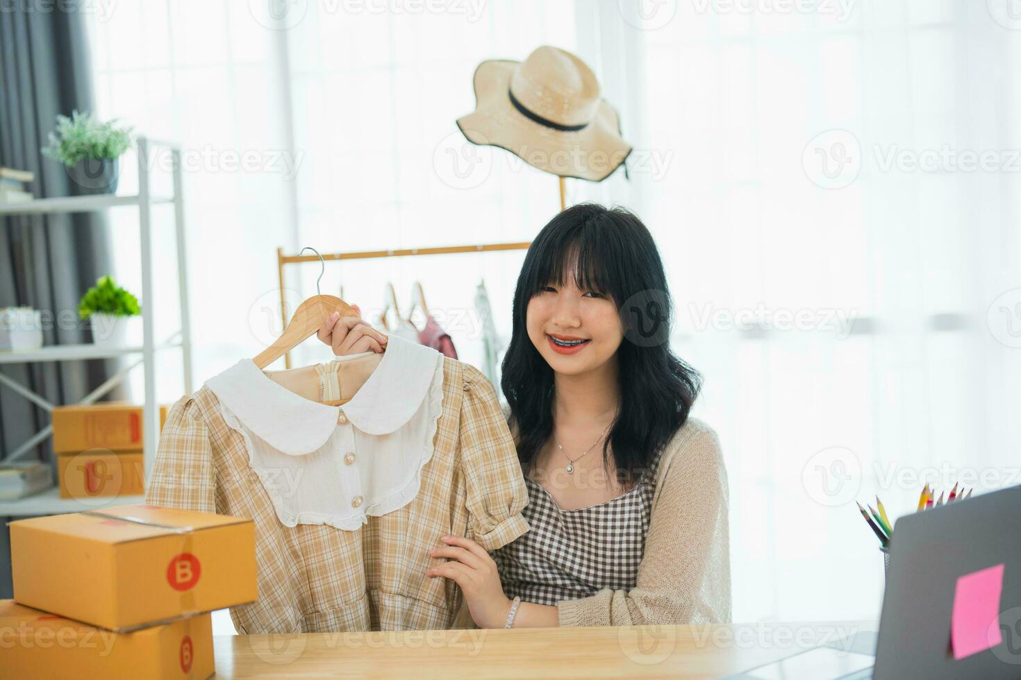 Asian woman steamming sell cloth shirt product online live at home. Young woman using mobile phone video call shows goods to customer and detail. Shopping online e-commerce buying and selling concept. photo
