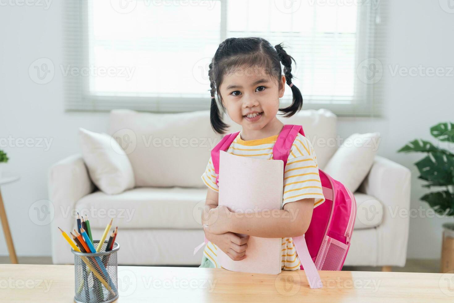 Asian kindergarten students smile backpack behind back a pink school bag and holding note book going to school for beginning of lessons. excited daughter are happy go school. Back to school concept. photo