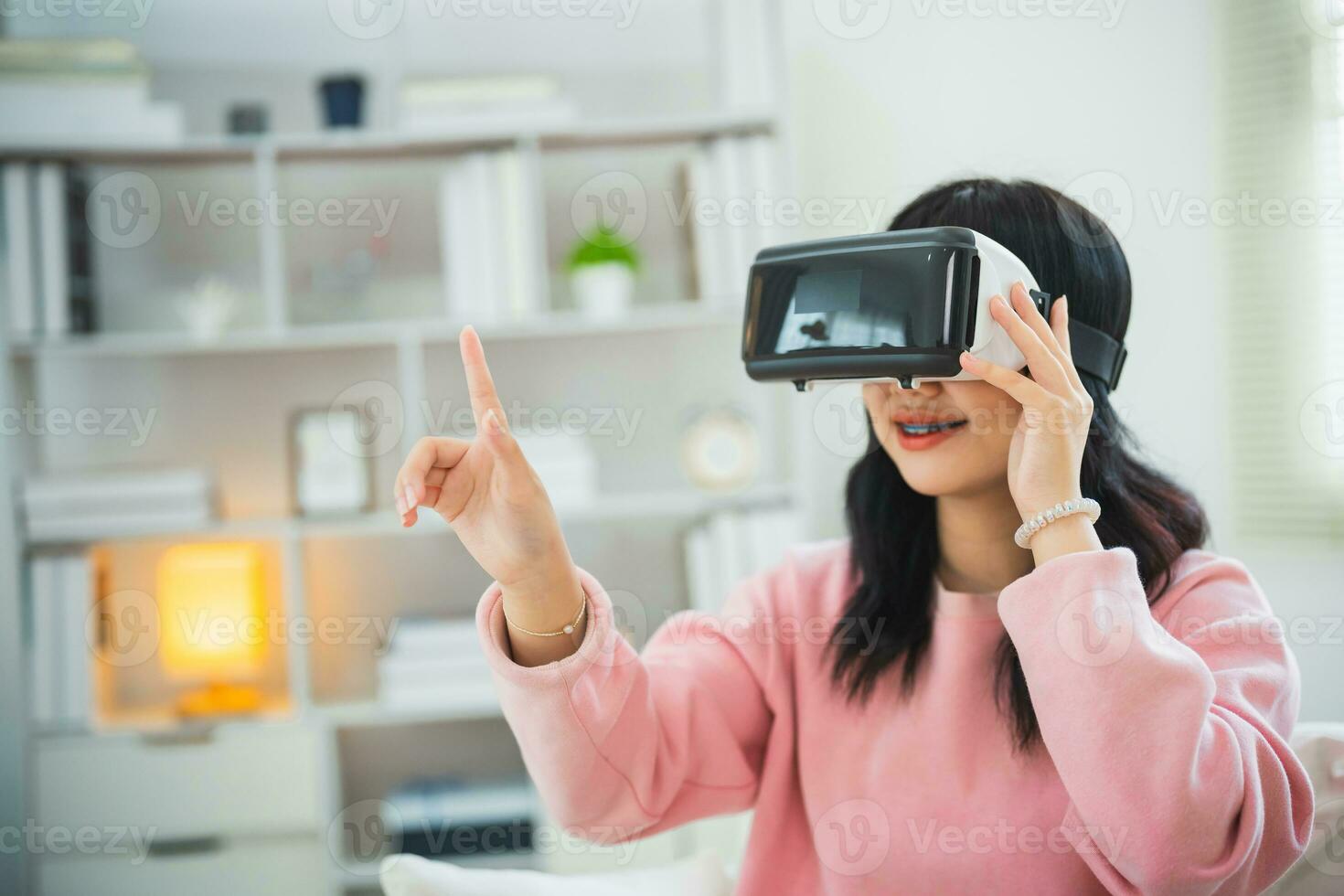 Asian woman smile and play VR game, 3D divice new innovation glasses for entertain in living room at home, asian woman joyful in house on holiday. Happy woman playing metaverse VR technology concept. photo