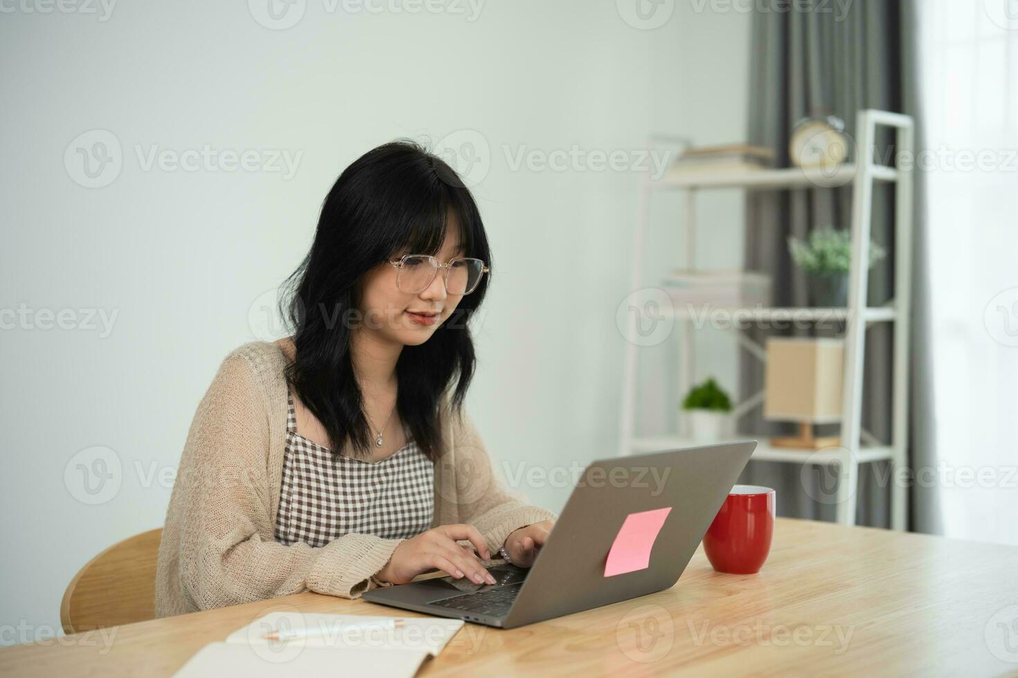 Asian freelance woman wearing glasses typing on keyboard and working on laptop on wooden table at home. Entrepreneur woman working for her business at living room home. Business work home concept. photo
