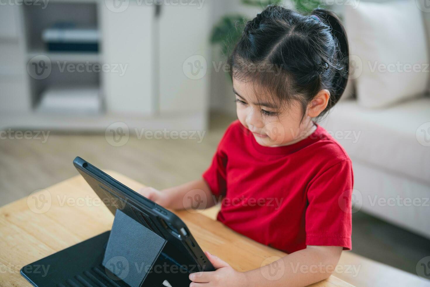 Asian child girl looking using and touch tablet display screen. Baby smiling funny time to use tablet. Too much screen time. Cute girl watching videos while tv, Internet addiction concept. photo