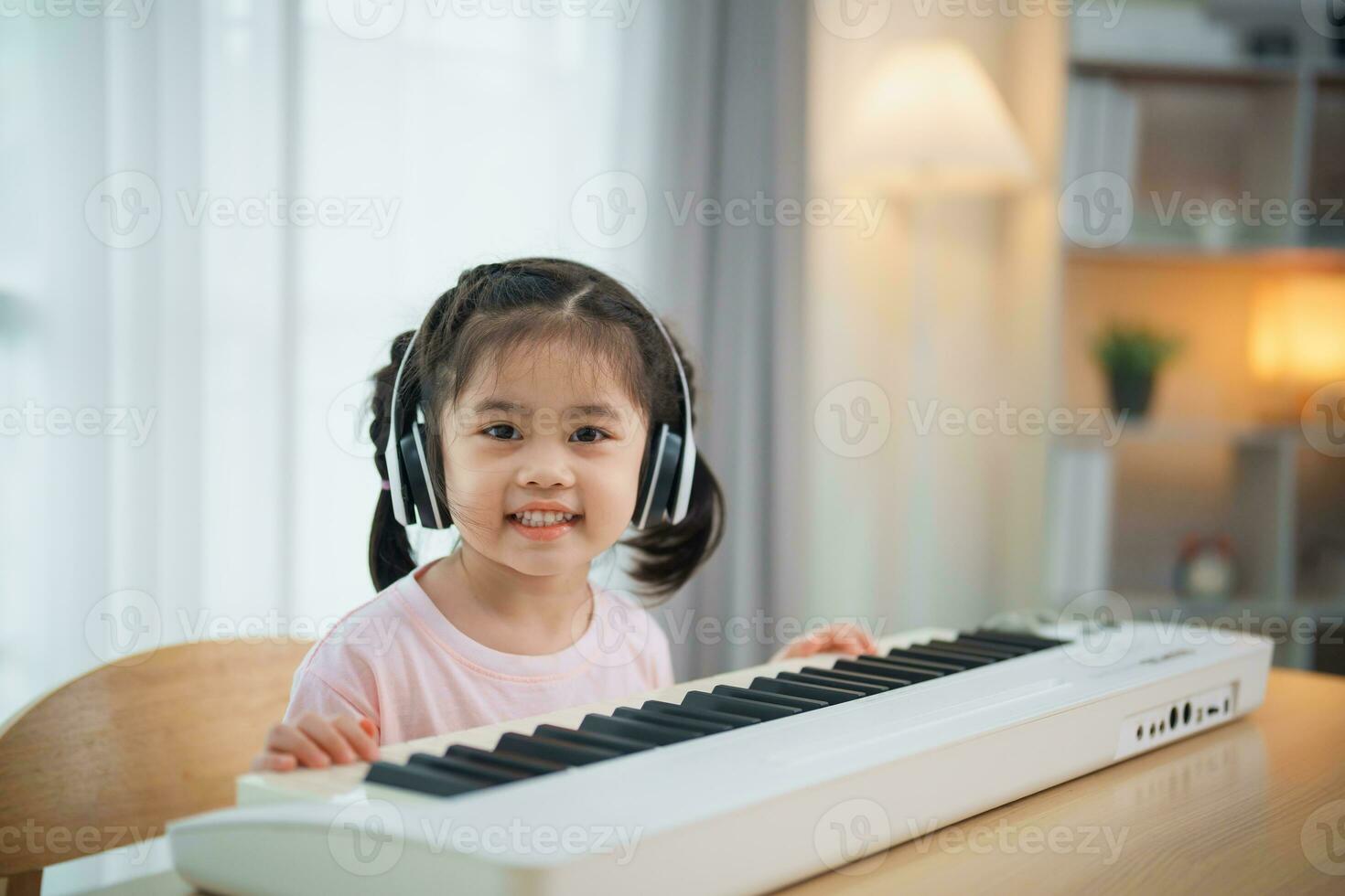 Asian cute girl smile and wearing white headphone playing learning online piano music in the living room at home. The idea of activities for the child at home during quarantine. Music learning study. photo