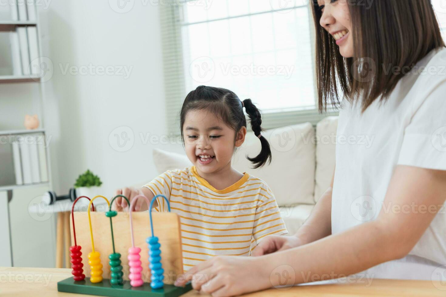 Young cute Asian girl and her parent mother mom is learning the abacus with colored beads to learn how to count sofa in the living room at home. Child baby girl development studing concept. photo