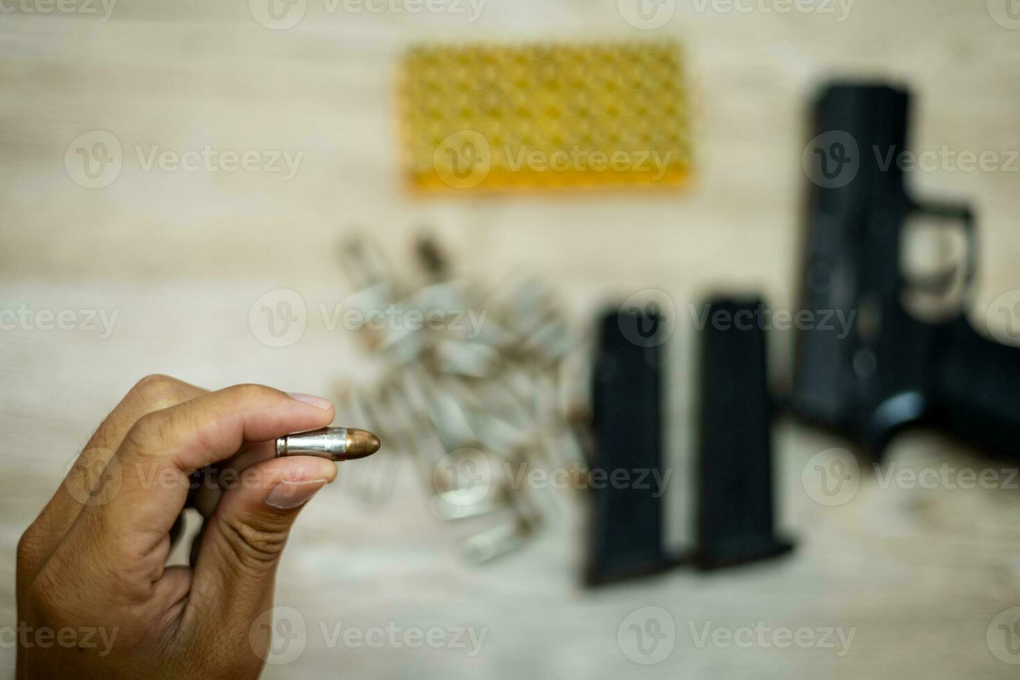 Male hand holding a bullet There's a pistol behind it, on a wooden table. photo