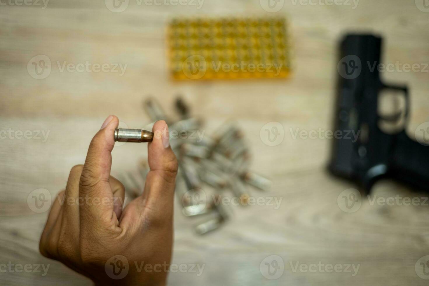 Male hand holding a bullet There's a pistol behind it, on a wooden table. photo