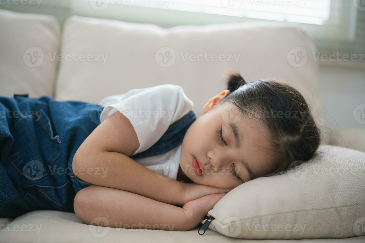 Cute little girl child sleeping on couch sofa with soft pillows at living room at home. Baby girl lying on the sofa couch bed. photo