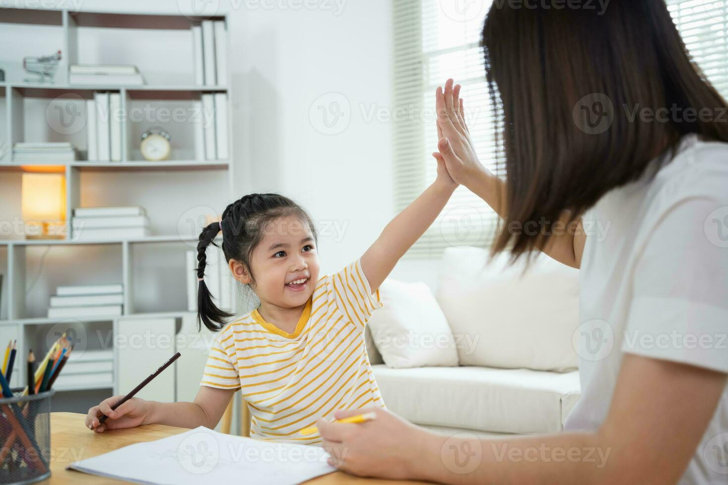 Cute little child and mom hands making give me five while painting with colorful paints. Asian girl and mother using crayon drawing color. Daughter and mom doing homework coloring cartoon characters. photo