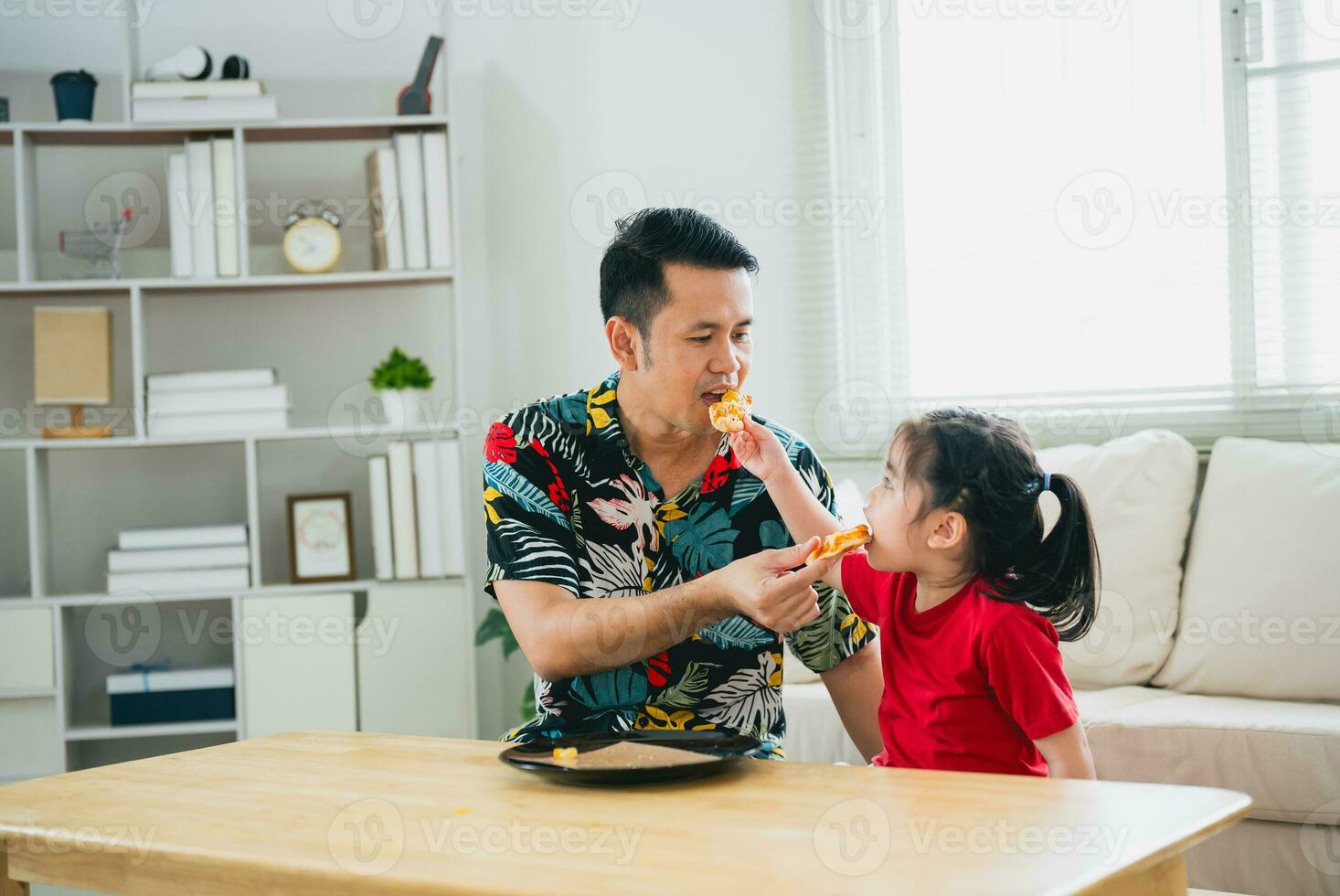 asiático contento niños niña y su padre alimentación comiendo Pizza y sonriente en el vivo habitación a hogar. niños niña y su papá comiendo y saboreo italiano hecho en casa Pizza en casa. foto
