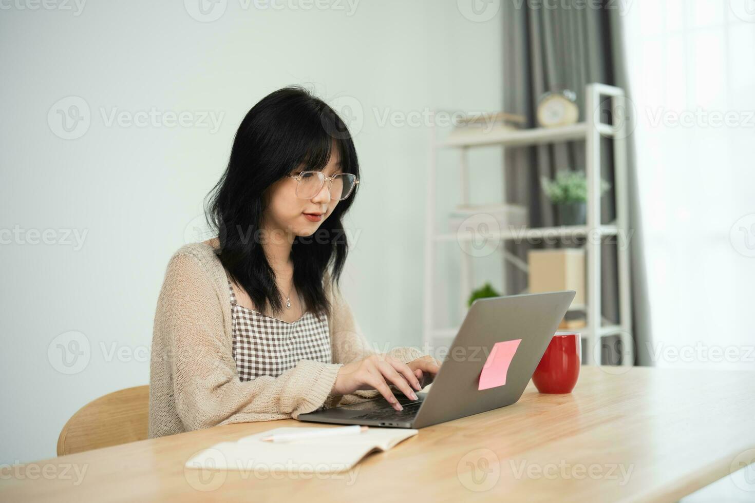 asiático Lanza libre mujer vistiendo lentes mecanografía en teclado y trabajando en ordenador portátil en de madera mesa a hogar. empresario mujer trabajando para su negocio a vivo habitación hogar. negocio trabajo hogar concepto. foto