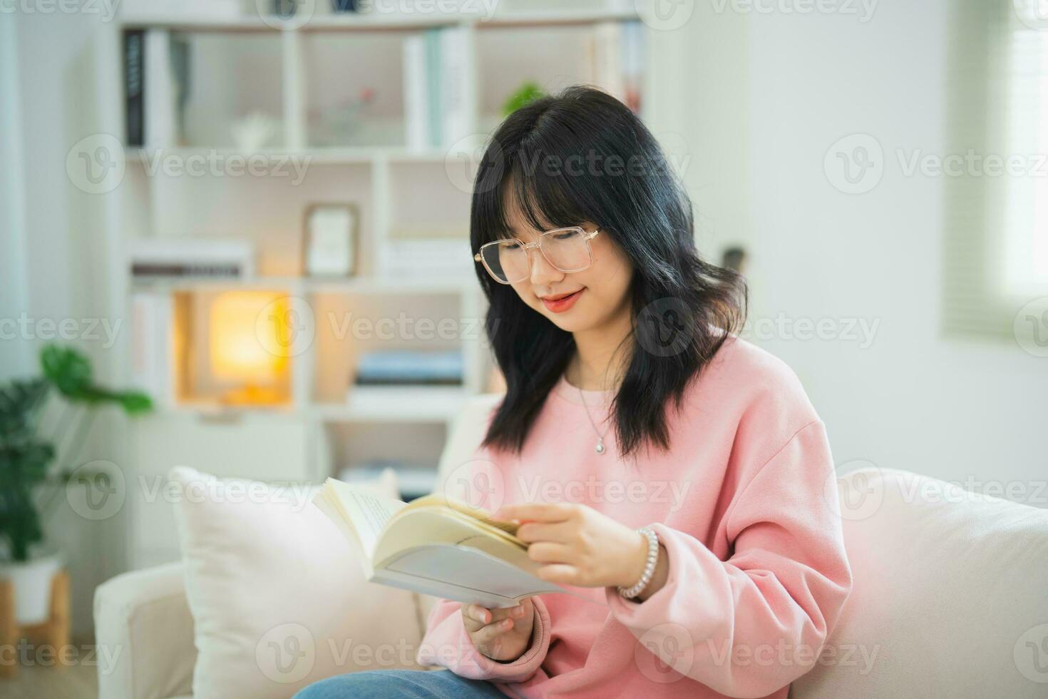 alegre contento asiático mujer sonriente y leyendo libro mientras sentado en sofá sofá en vivo habitación a hogar. asiático mujer relajarse leyendo libro sonrisa a sofá en el casa. actividad pasatiempo a casa concepto. foto
