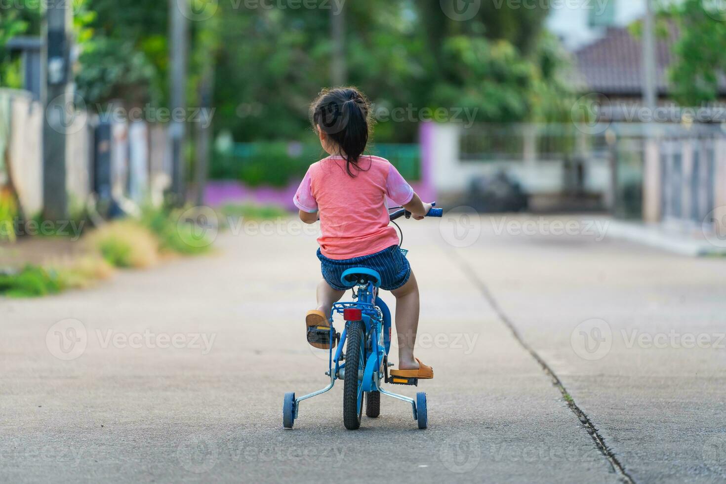 Backside of asian toddler girl child learning to ride bicycle in sunny summer day, kid cycling at park, baby sport concept photo