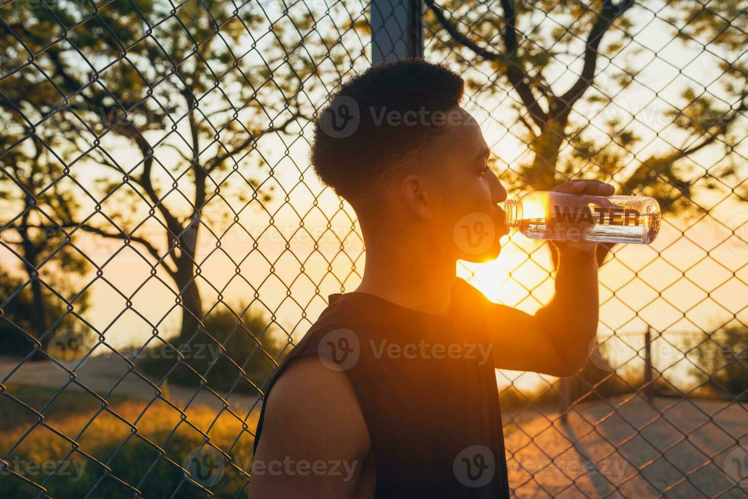 negro hombre haciendo Deportes en mañana, Bebiendo agua en baloncesto Corte en amanecer foto