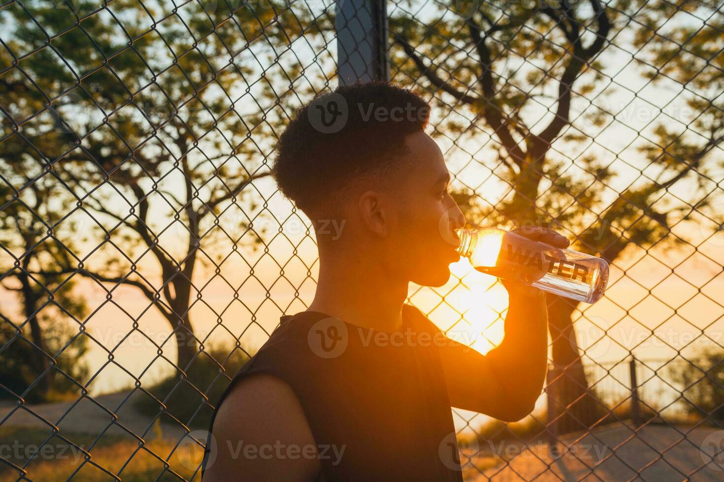 negro hombre haciendo Deportes en mañana, Bebiendo agua en baloncesto Corte en amanecer foto