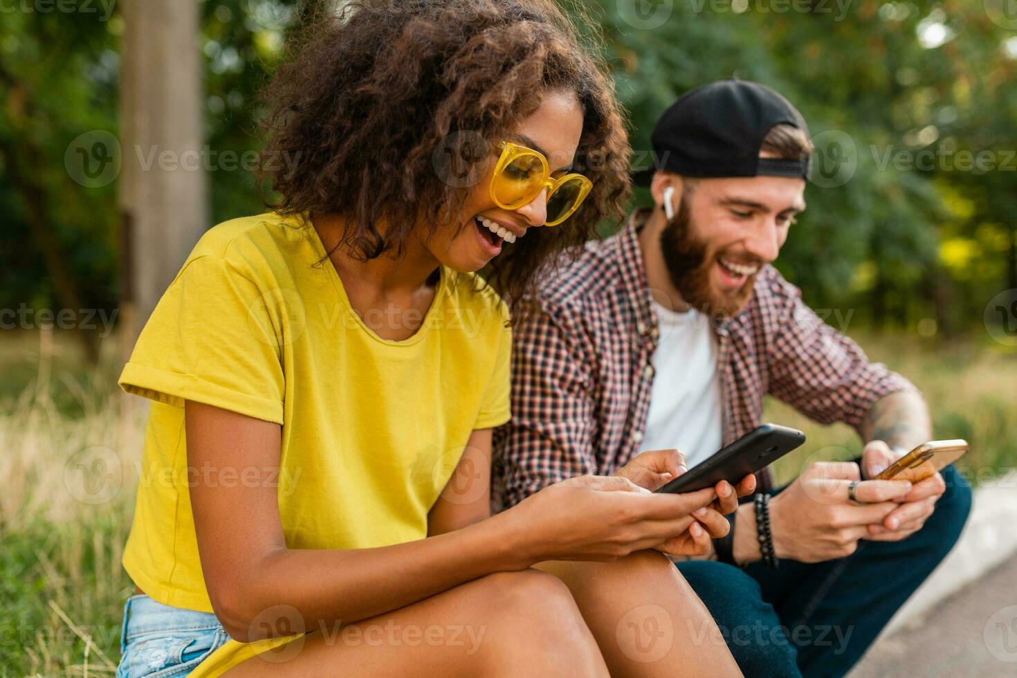 happy young smiling friends sitting park using smartphones photo