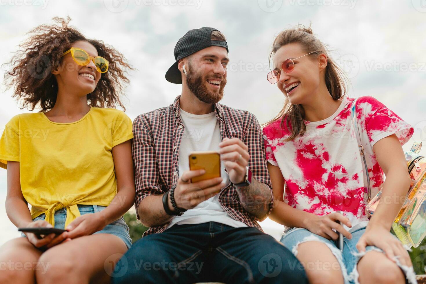 happy young company of smiling friends sitting in park photo