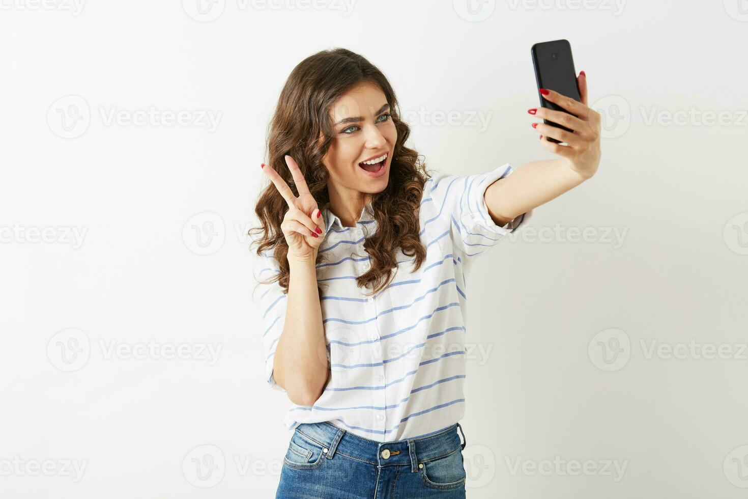beautiful woman with funny face expression making selfie photo on mobile phone, smiling, happy, islolated, curly hair, positive mood, student hipster style