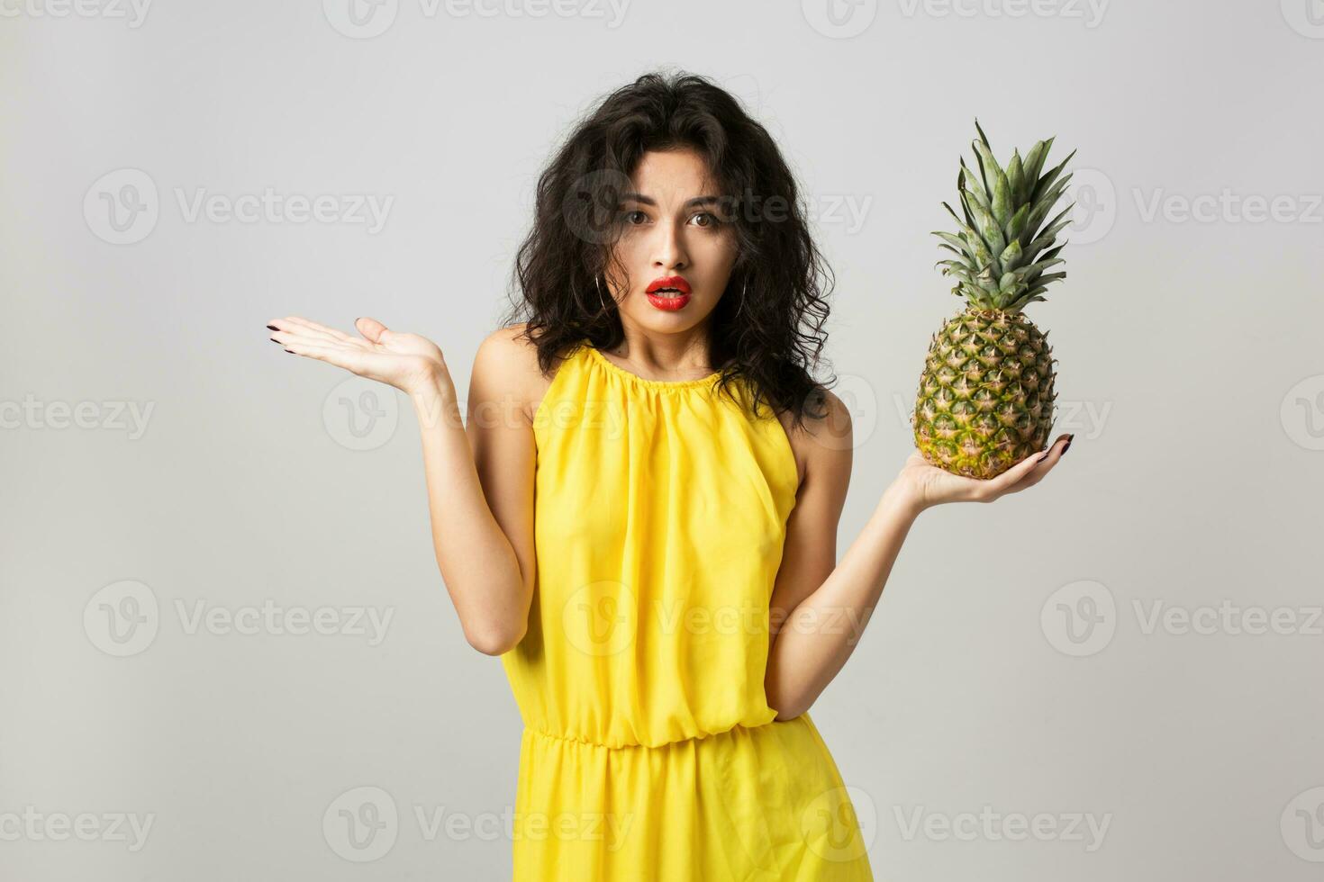 portrait of young surprised pretty woman in yellow dress, holding pineapple, funny emotion, shocked face expression, summer style, fruit diet, looking in camera, mixed race, isolated, holding hands up photo
