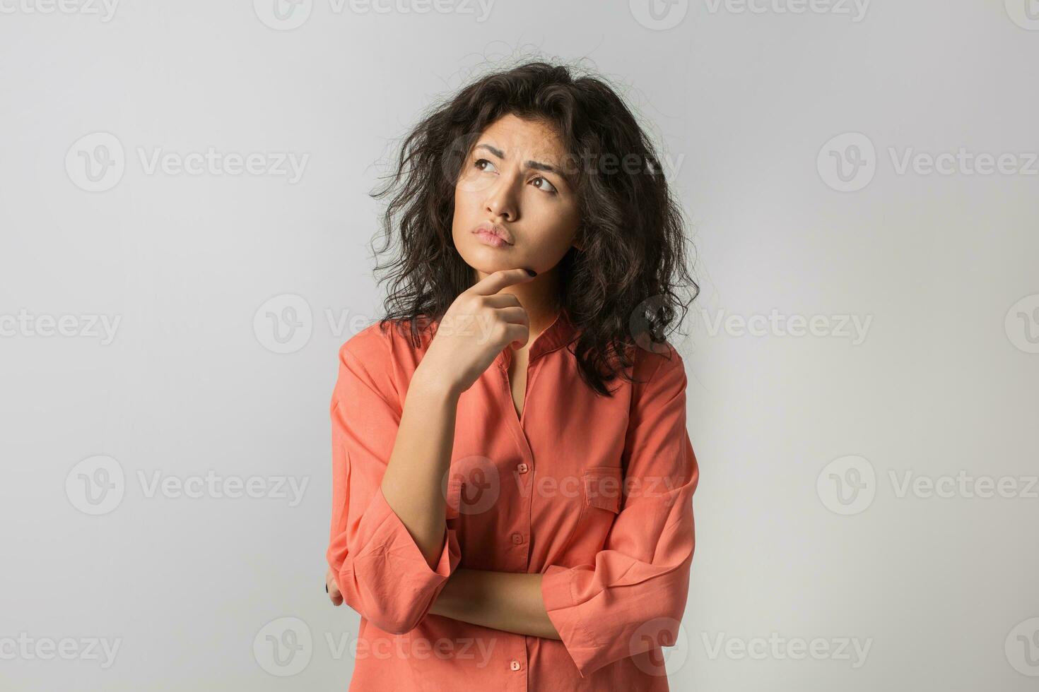 portrait of young thoughtful brunette woman in orange shirt, summer style, frustrated face expression, sad emotion, looking up, thinking, problem, mixed race, touching her chin, isolated, frowning photo