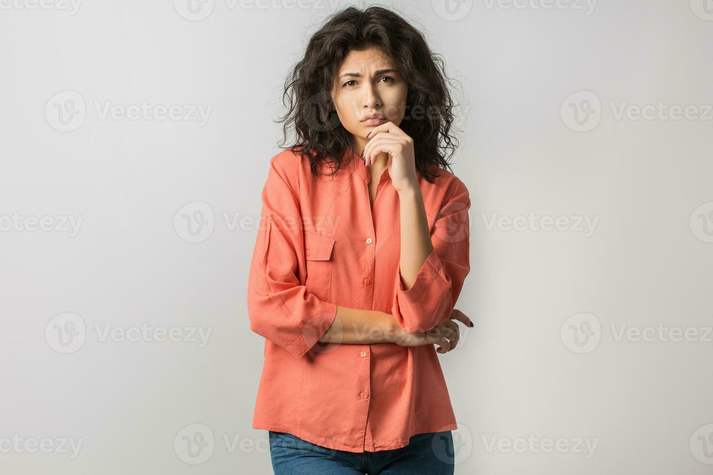 portrait of young thoughtful brunette woman in orange shirt, curly hair, summer style, frustrated face expression, sad emotion, looking in camera, thinking, problem, idea, mixed race, isolated photo