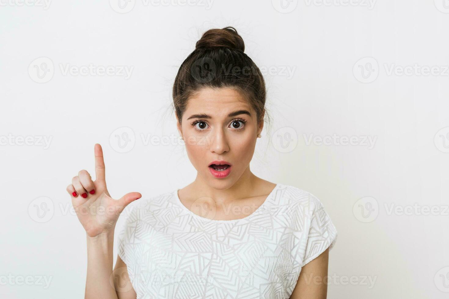 cerca arriba retrato de joven conmocionado mujer en blanco blusa señalando dedo arriba, emocional, teniendo idea, sorprendido cara expresión, mirando dentro cámara, aislado en estudio antecedentes foto