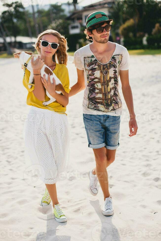 hipster joven elegante hipster Pareja en amor caminando jugando perro perrito Jack Russell en tropical playa, blanco arena, frio atuendo, romántico ánimo, teniendo divertido, soleado, hombre mujer juntos, vacaciones foto