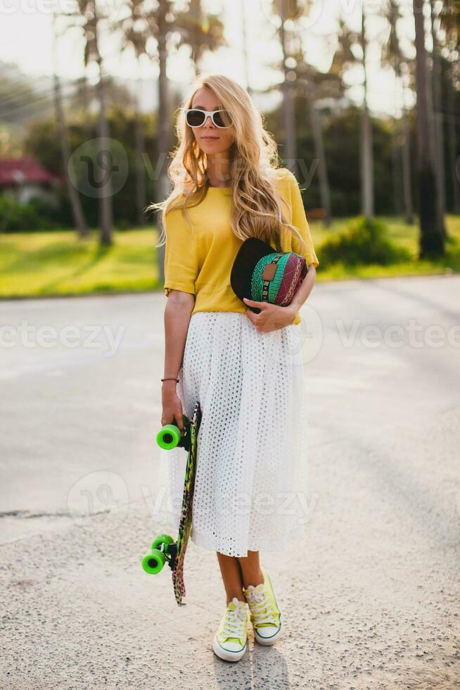 hipster frio mujer con patinar tablero y gorra posando sonriente en vacaciones foto