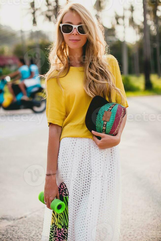 hipster frio mujer con patinar tablero y gorra posando sonriente en vacaciones foto