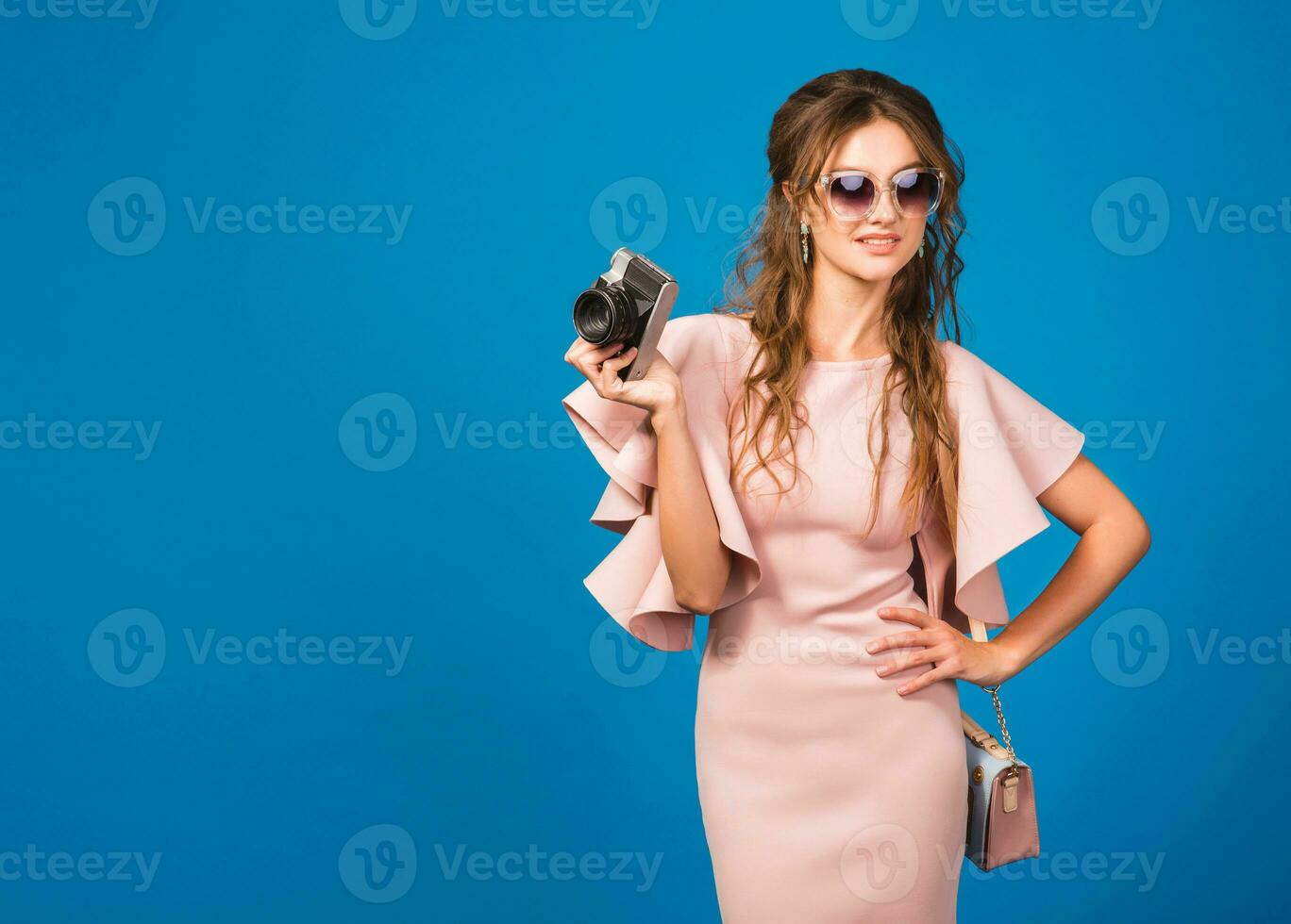 young stylish sexy woman in pink luxury dress taking pictures on vintage camera photo