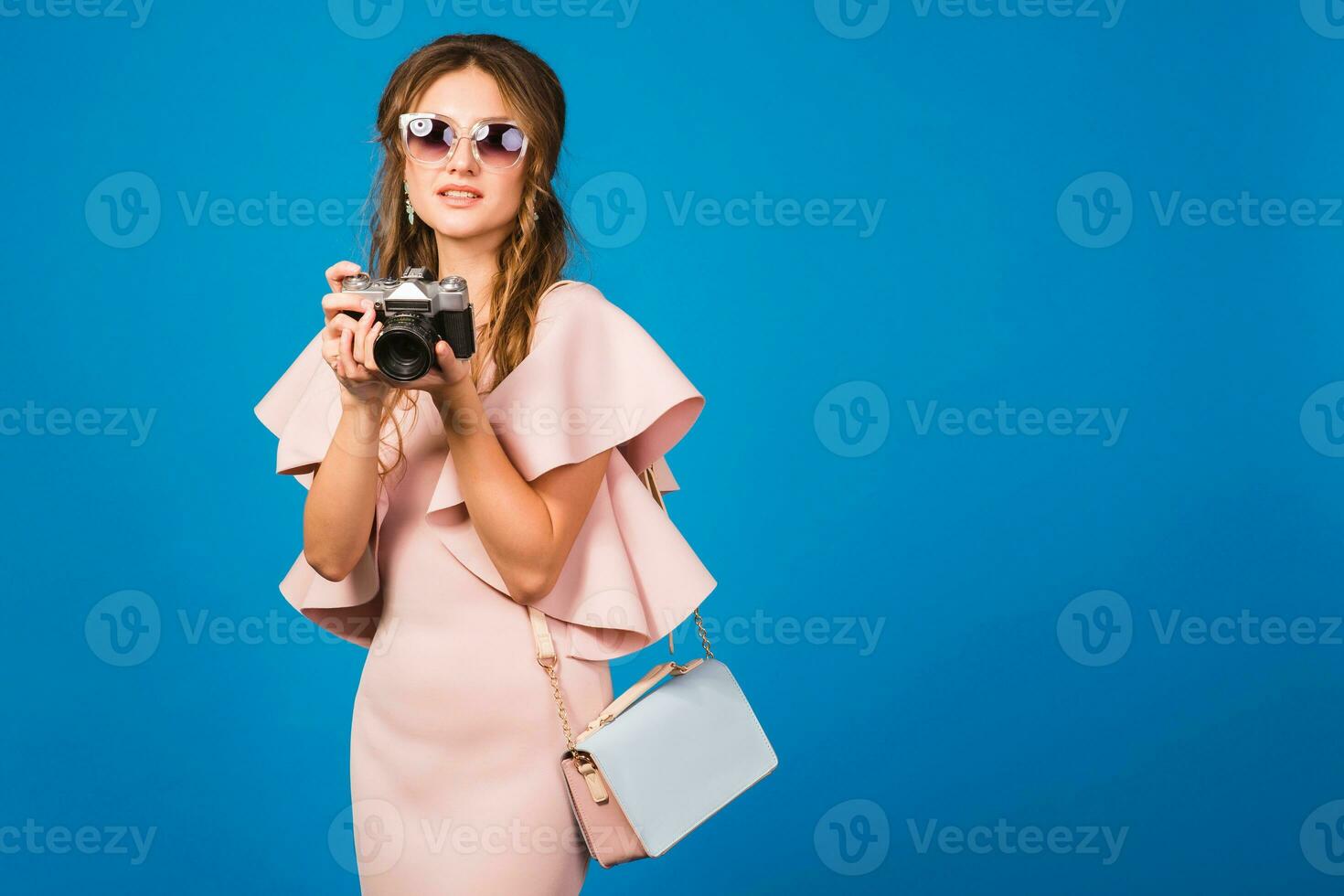 young stylish sexy woman in pink luxury dress taking pictures on vintage camera photo