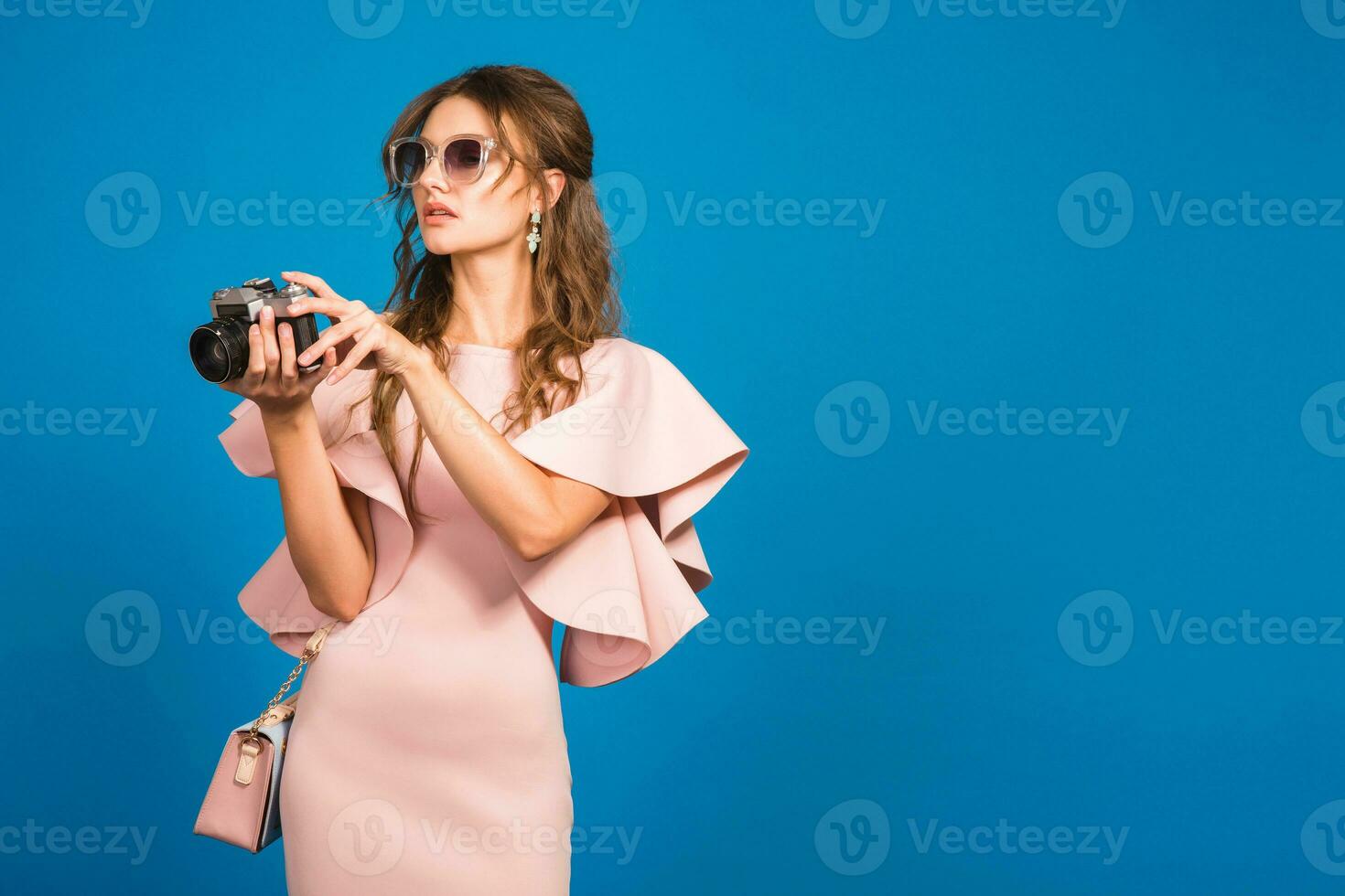 young stylish sexy woman in pink luxury dress taking pictures on vintage camera photo