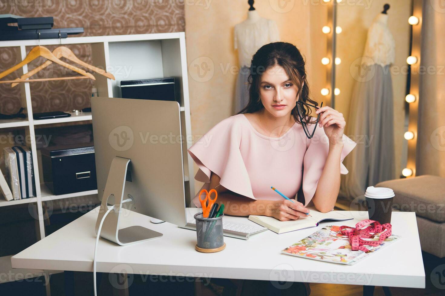 young stylish sexy woman in pink luxury dress fashion designer working at office on computer photo