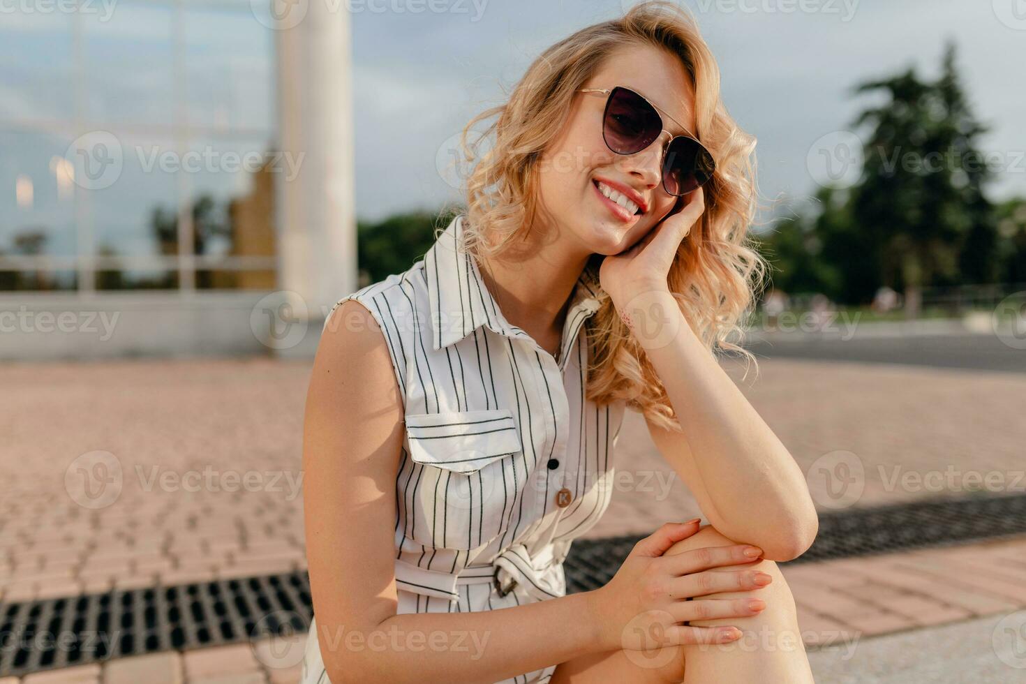 young attractive cute stylish blonde woman sitting in city street in summer fashion style photo