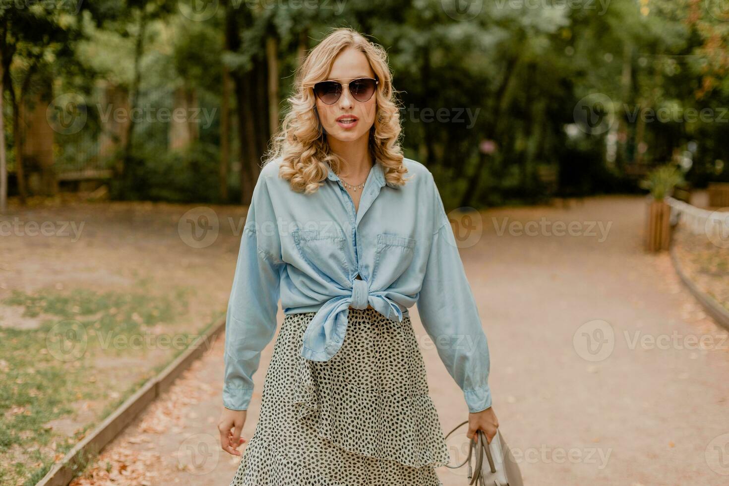 attractive blond smiling woman walking in park in stylish outfit photo